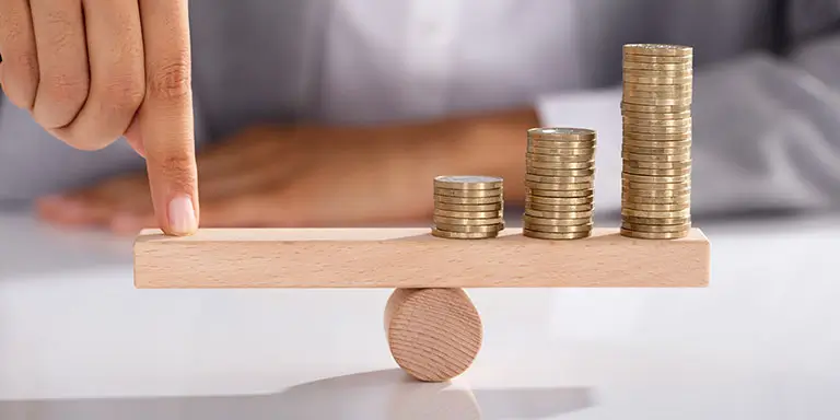A person holding a stack of coins on a wooden balance, symbolizing financial stability and careful management