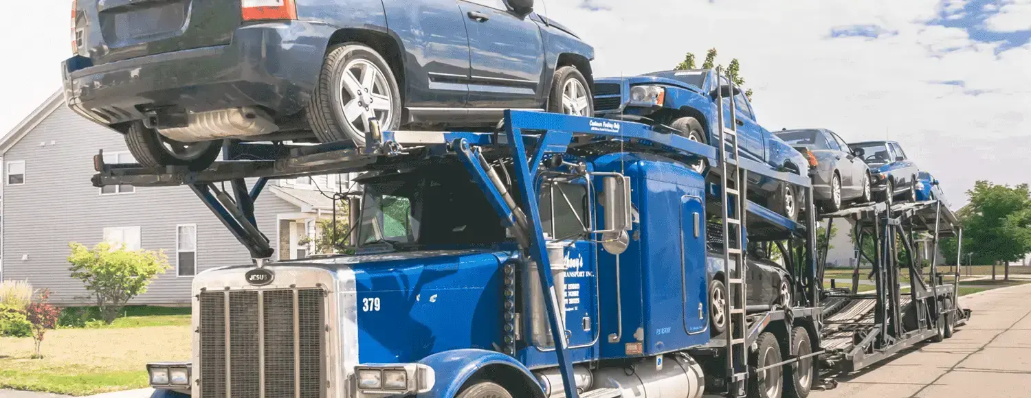 A blue semi truck carrying several cars on a flatbed trailer.