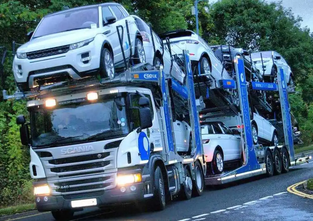 A  white Scania car carrier truck transports several cars on a wet road