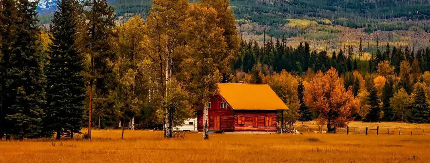 A log cabin nestled in a meadow, with the majestic peaks of the Rocky Mountains towering in the distance