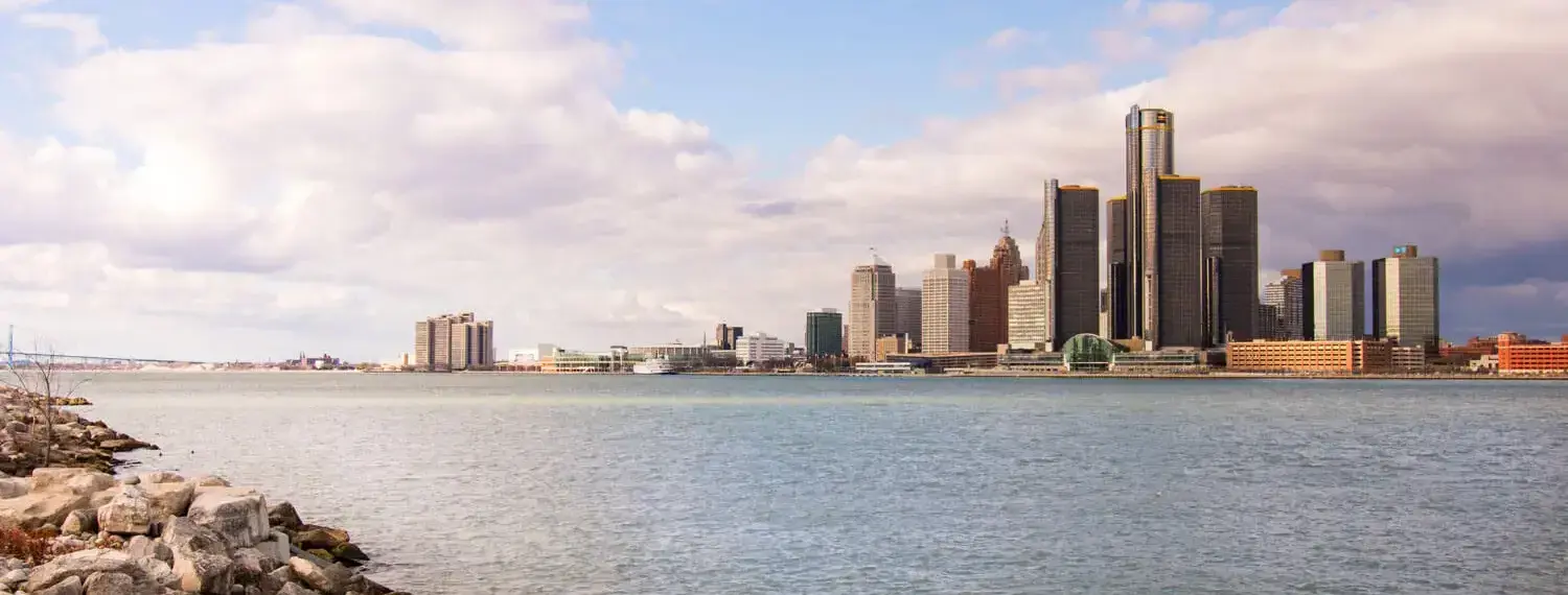 A daytime view of Detroit, Michigan, across the Detroit River. The Renaissance Center, a collection of interconnected skyscrapers, dominates the skyline.