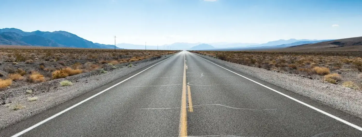 A long, straight asphalt road stretches through a desolate Nevada desert landscape.