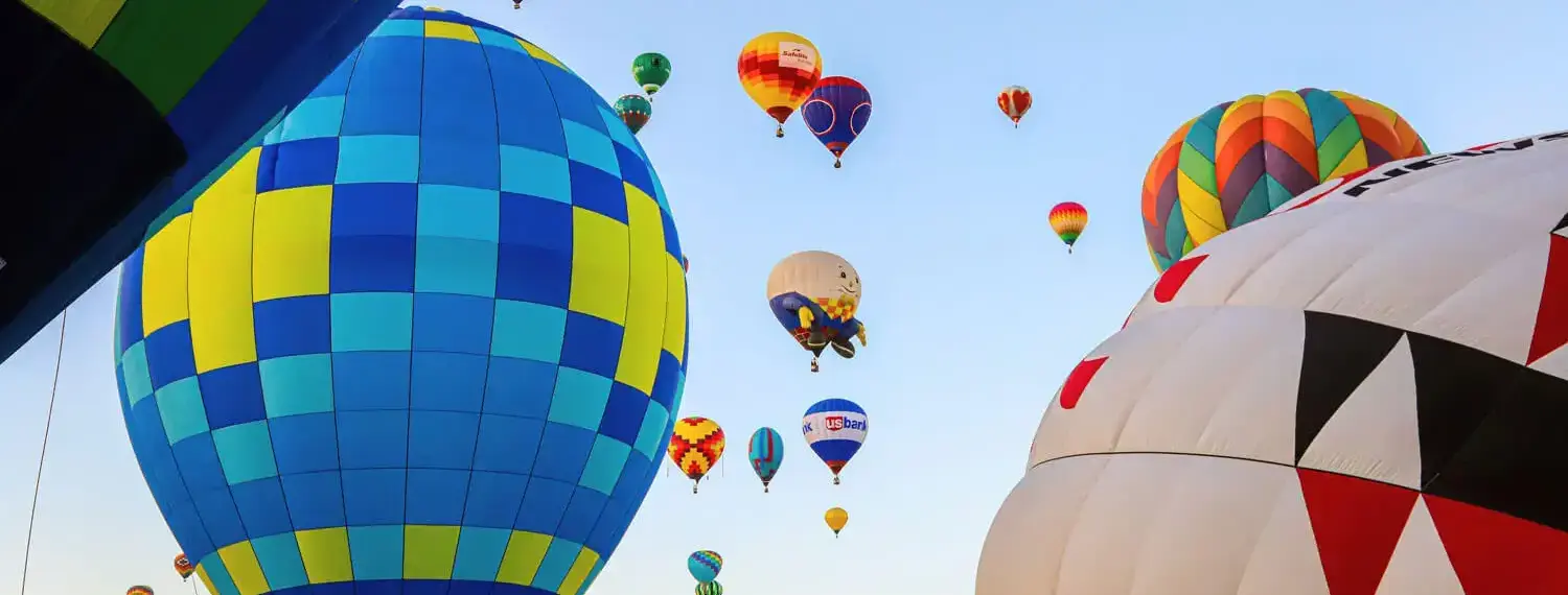 Colorful hot air balloons ascending into the clear blue sky of New Mexico.