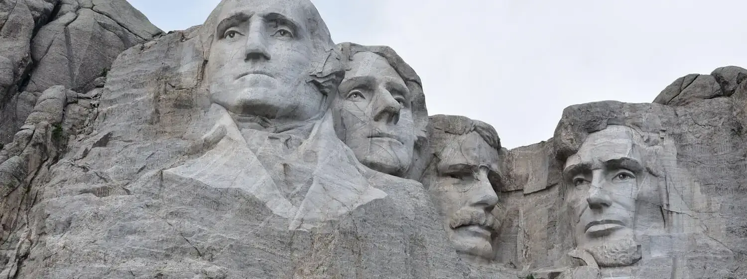 A photograph capturing the faces of former Presidents carved into the towering granite of Mount Rushmore, seen from a perspective pointing upwards.
